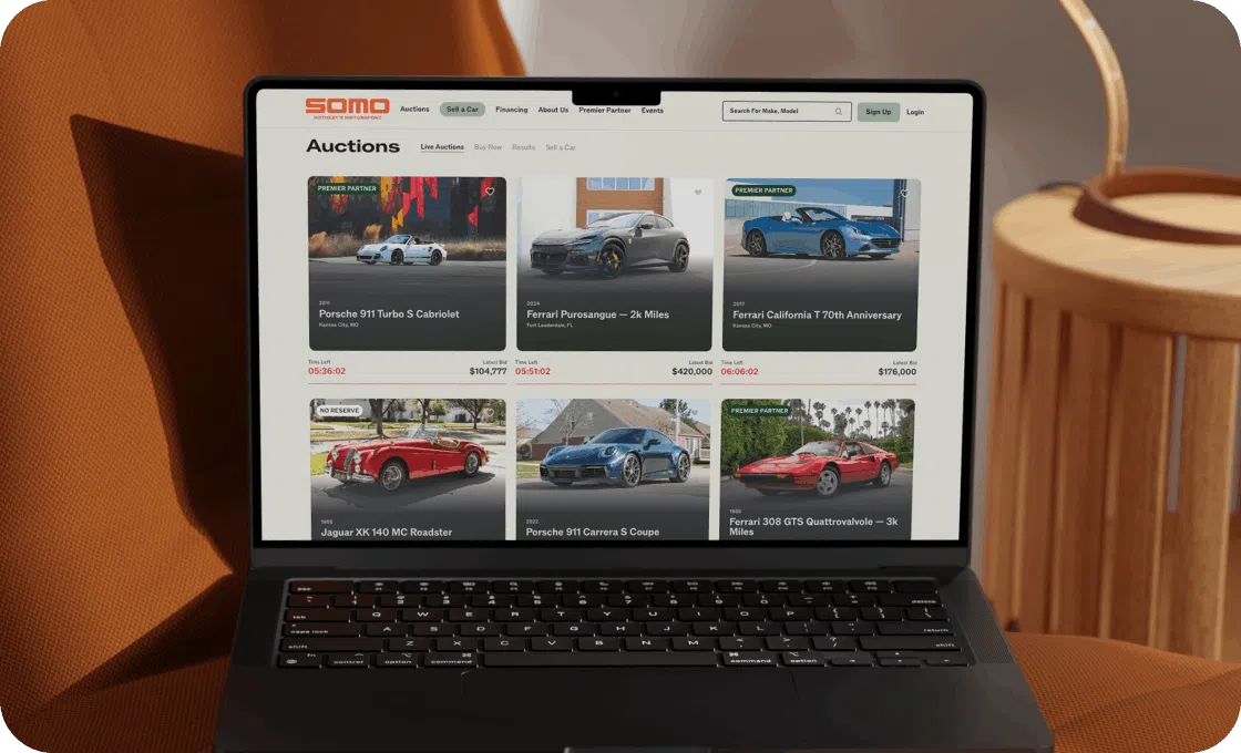 A laptop displays an online car auction page with listings of various luxury cars. The background has warm brown tones, creating a cozy atmosphere.